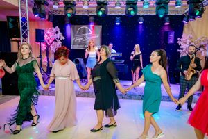 Guests hold hands in a dance circle under professional lighting at an indoor celebration.