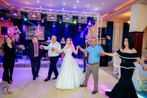 Wedding party forms dance circle under professional lighting setup at indoor reception venue.