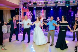 Wedding guests dancing in a reception hall with colorful purple and blue lighting and stage equipment.