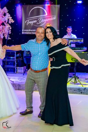 Couple posing in front of Troupe Dynamica band logo sign at wedding reception.
