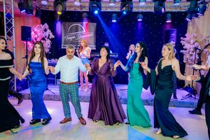 Group dancing together at wedding reception with colorful formal attire under dramatic lighting.
