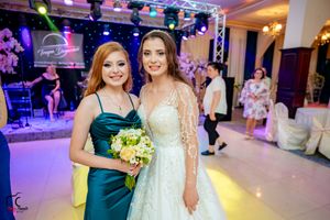 A wedding celebration with a bridesmaid in emerald silk gown holding yellow flowers beside a bride in lace dress.