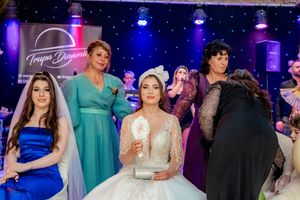 Festive wedding reception scene with guests in evening wear under vibrant blue and purple stage lighting.