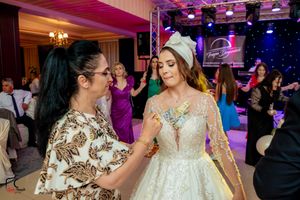 A bride in an elegant white gown interacts with a guest during a wedding reception with colorful lighting.