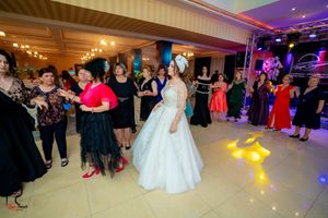 Guests gather on the dance floor around a bride in a white ballgown during a wedding reception.