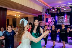 Wedding guests dance together under purple lighting and stage equipment at an elegant reception venue.