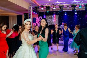 Wedding celebration on dance floor with guests in colorful attire under purple stage lighting.