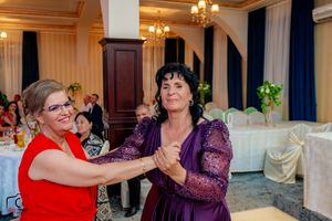 Two guests dance together in a ballroom with elegant chandeliers and white table settings.