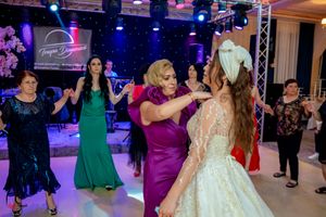 Formal event with guests in colorful dresses dancing under purple mood lighting.