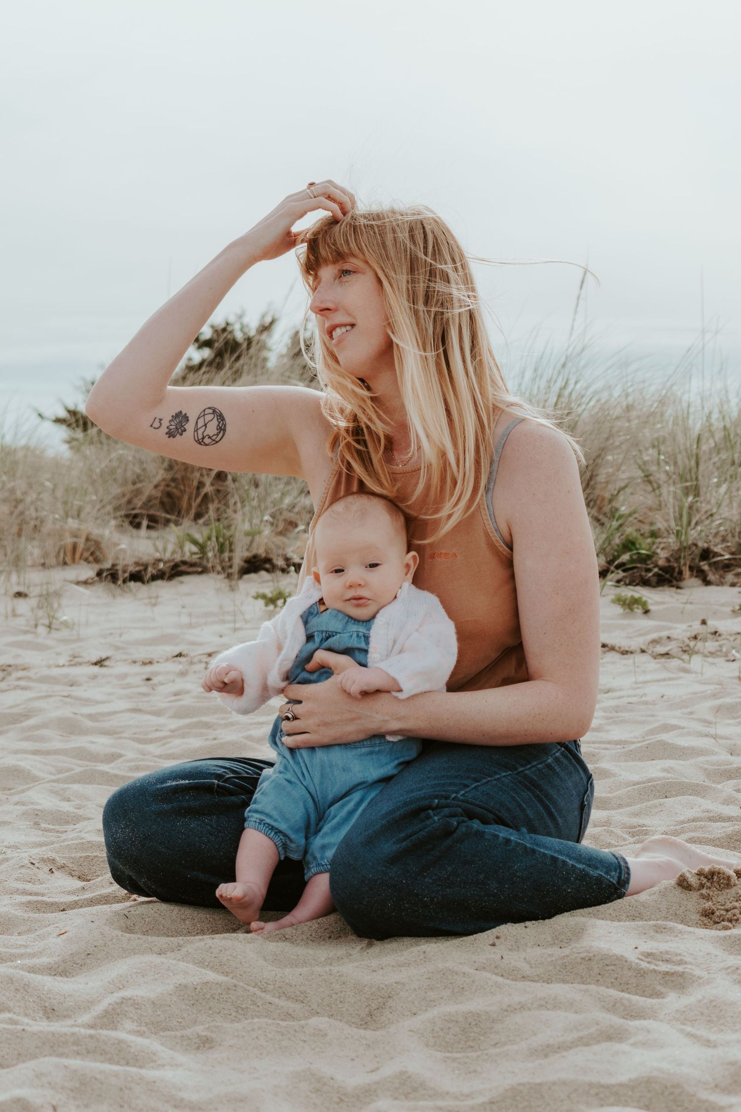 A parent and baby sitting together on sandy beach during a serene sunset photoshoot.