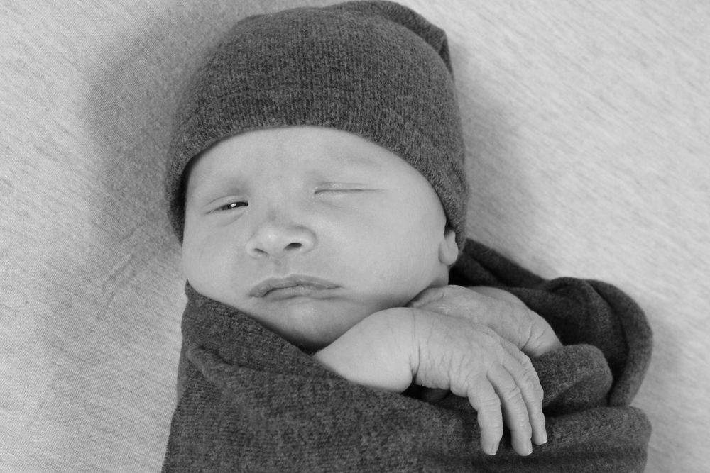 Black and white portrait of sleeping infant wearing dark beanie hat.