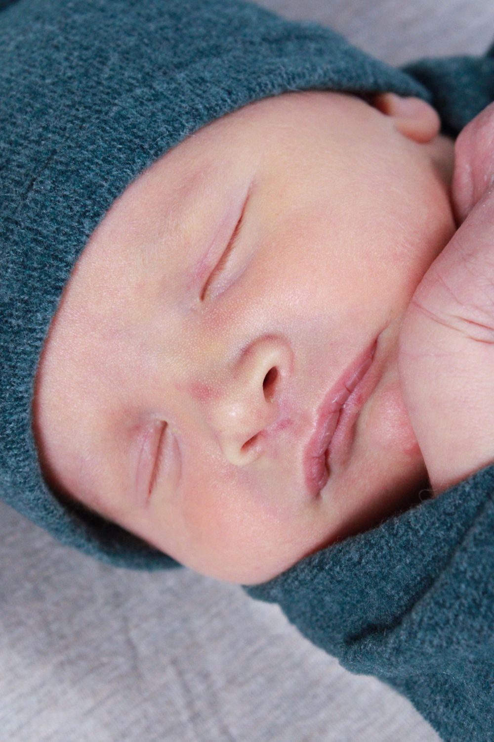 Peaceful sleeping newborn wearing teal hat against white background.
