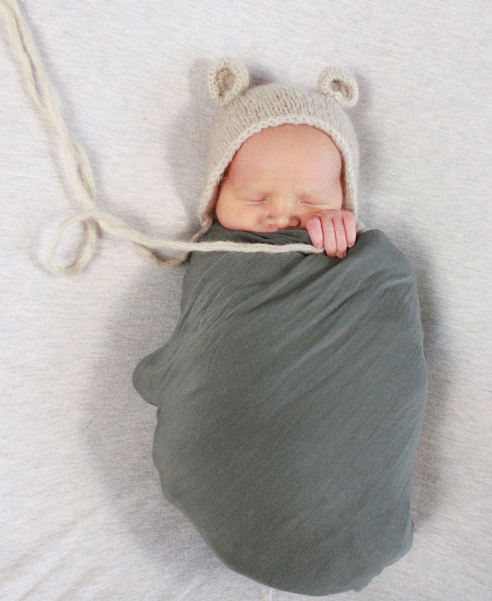 Sleeping newborn swaddled in gray wrap wearing knit bear hat.