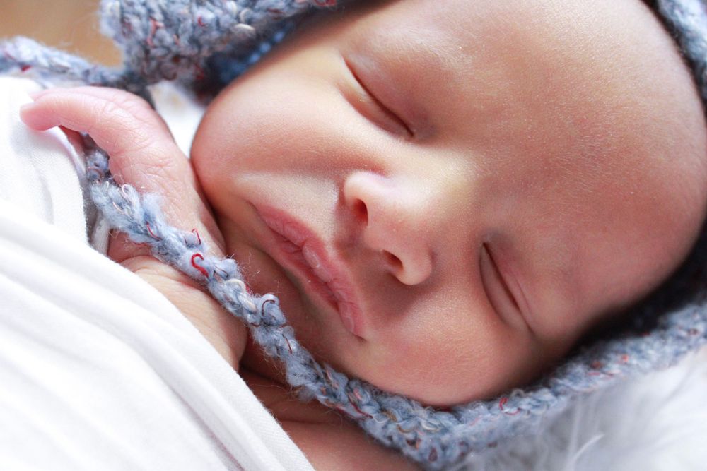 Serene sleeping baby wrapped in soft blue knitted blanket.