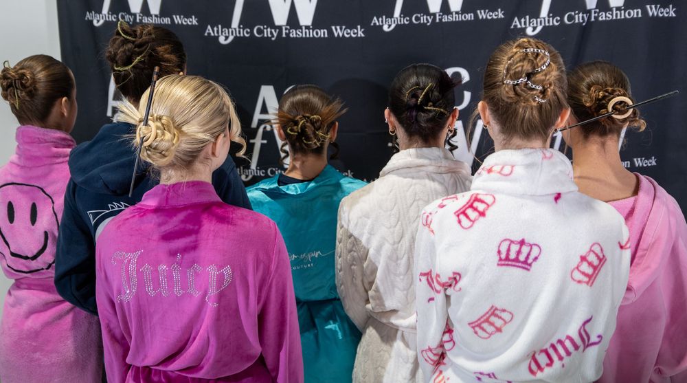 A group of people wearing pink jackets stand in front of a black wall with text.