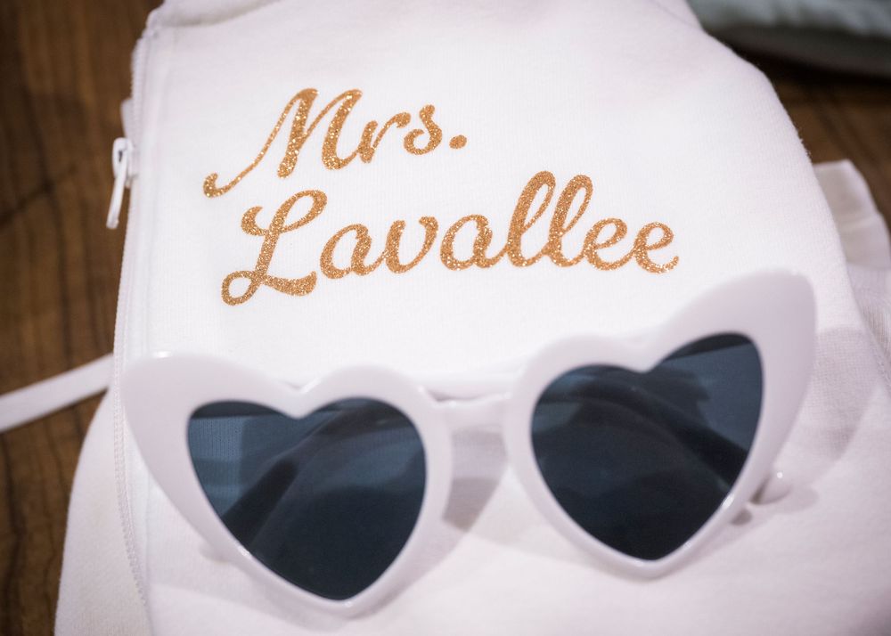 A white baseball cap with embroidered text "Mrs. Lavallee" and white heart-shaped sunglasses arranged together.