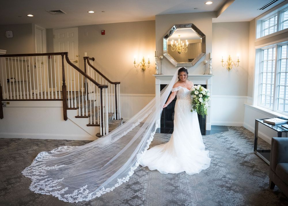 An elegant wedding dress with long lace train and veil in a luxurious interior setting with staircase and wall sconces.