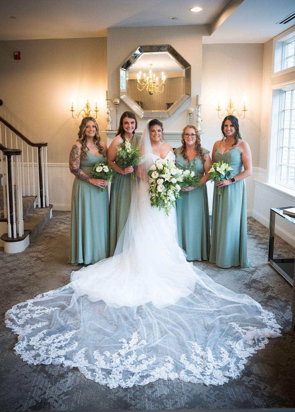 A bridal party wearing seafoam green dresses poses together, showcasing an elegant lace wedding gown with flowing train.