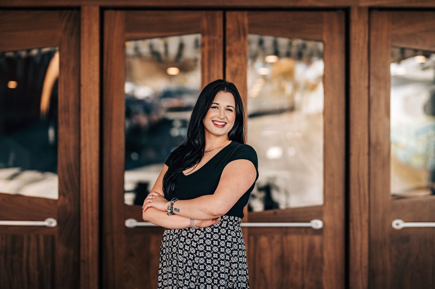Professional portrait in black top and patterned skirt against wooden doors.