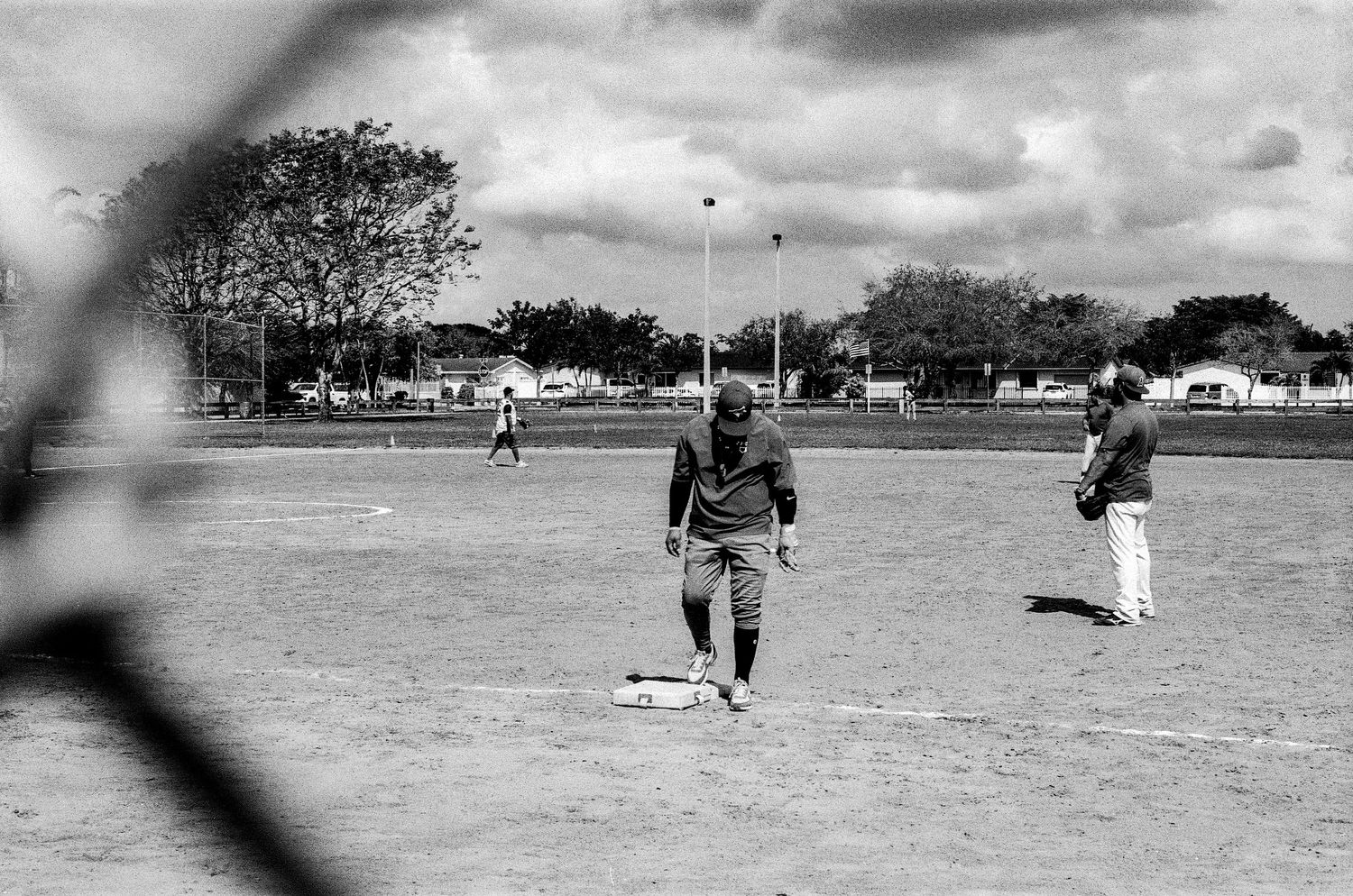 A black and white vintage baseball scene shows players on a dusty field with trees in the background.