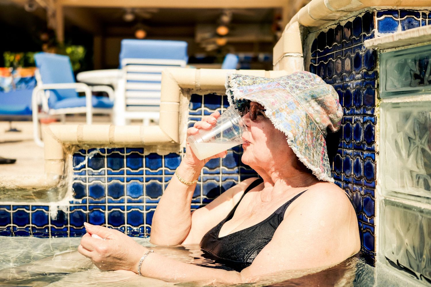 Someone wearing a sun hat relaxes in a swimming pool on a sunny day while seeking shade.