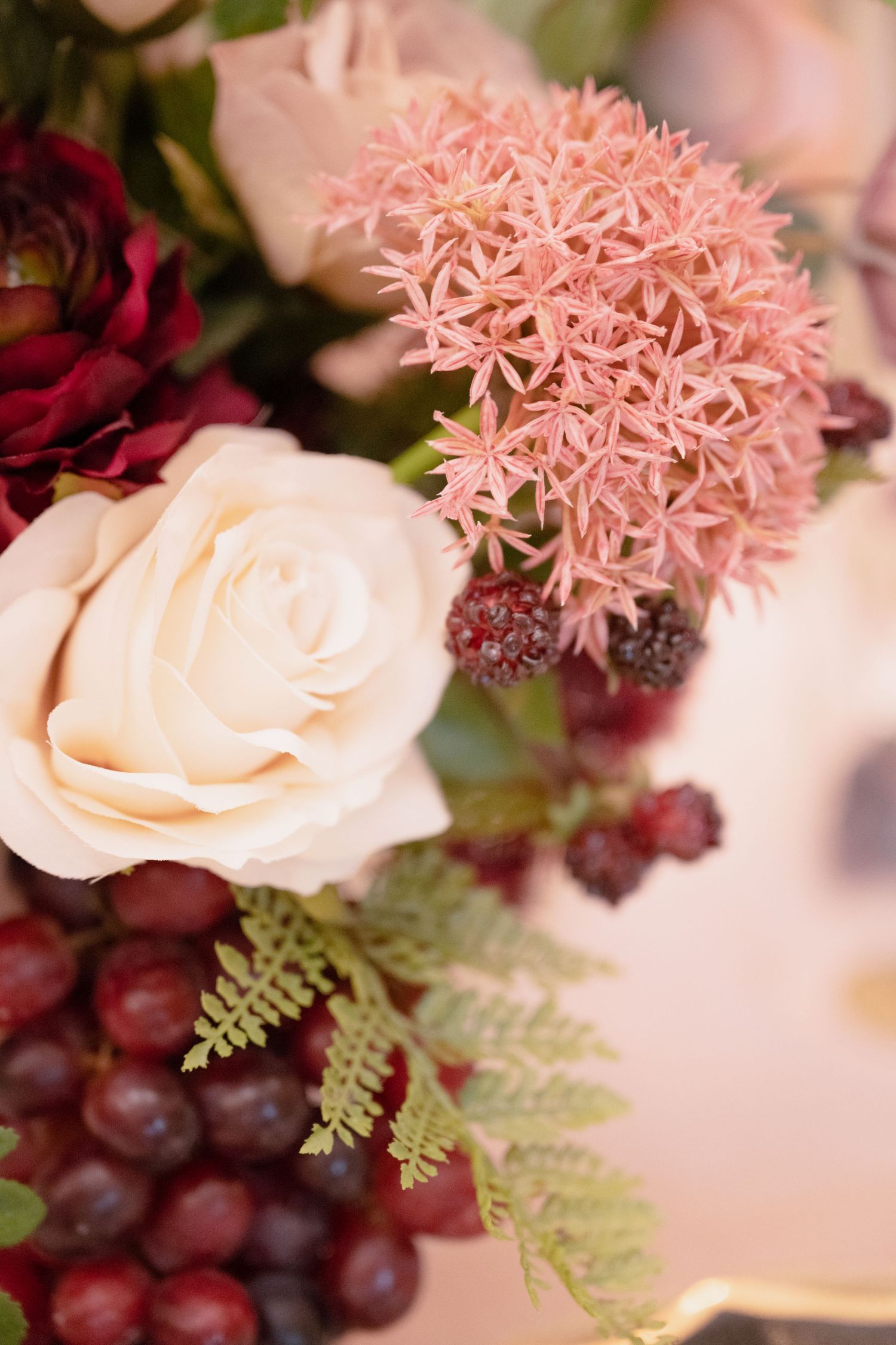 A close-up of a beautiful wedding floral arrangement with cream roses, burgundy flowers and berries.
