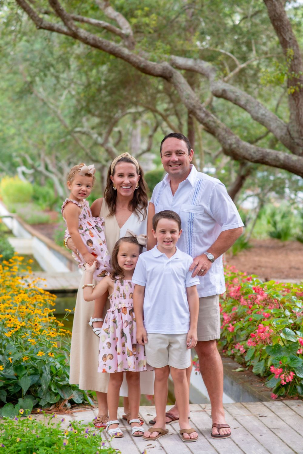 Family poses together on garden path surrounded by colorful flowers and twisted tree branches.