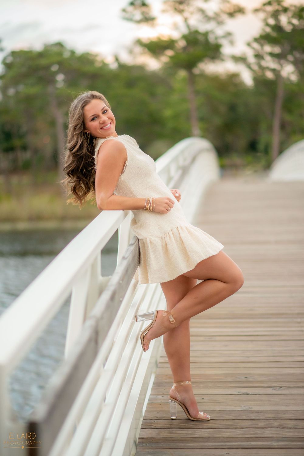 A person in a cream-colored dress poses on a wooden dock over water during golden hour.