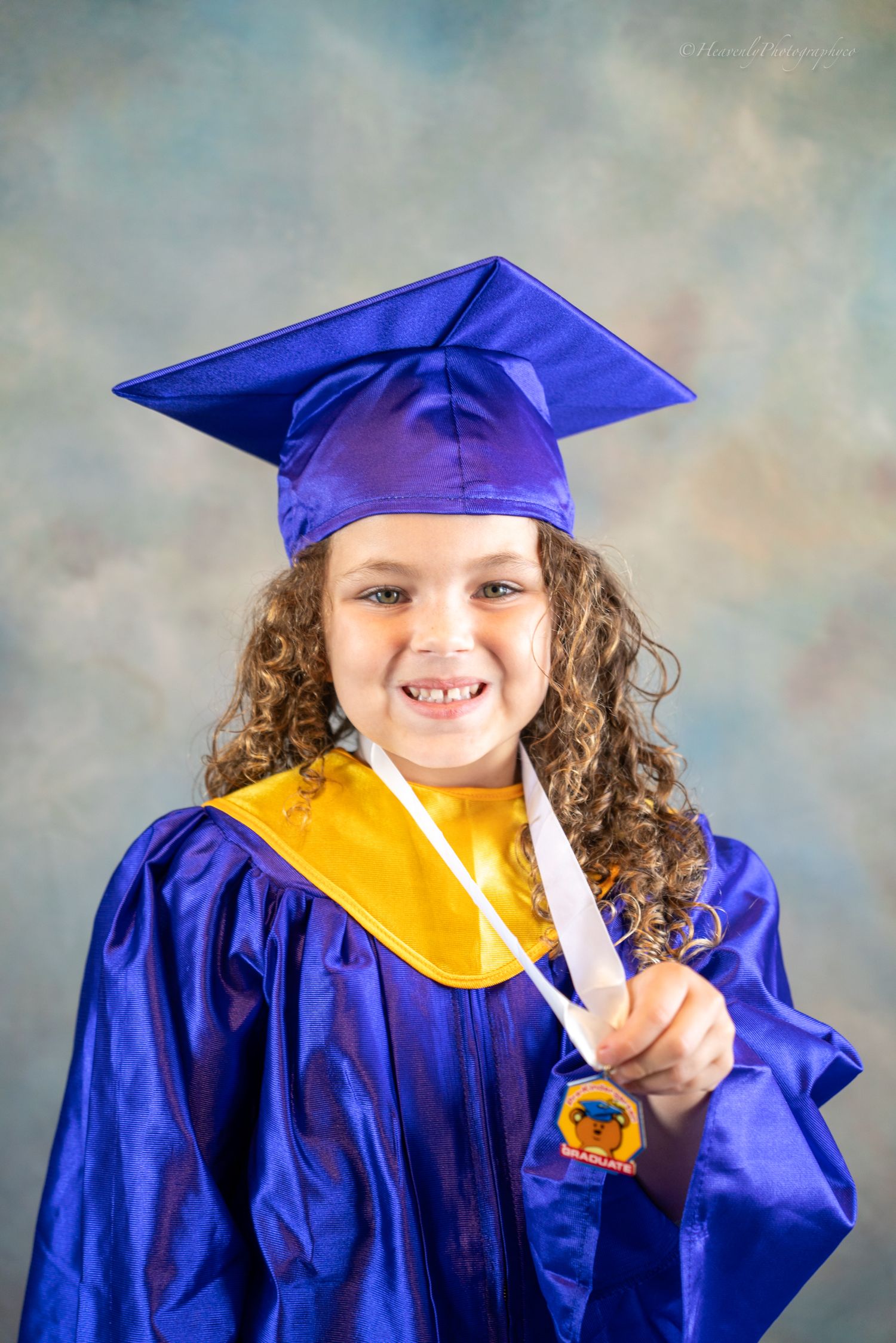 Young graduate in blue cap and gown with yellow stole smiling for photos.