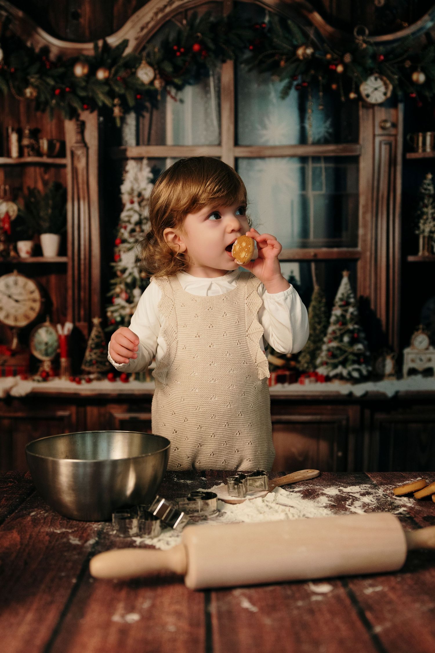 A small child tastes a cookie while baking in a festive kitchen decorated for Christmas with rolling pin and flour.