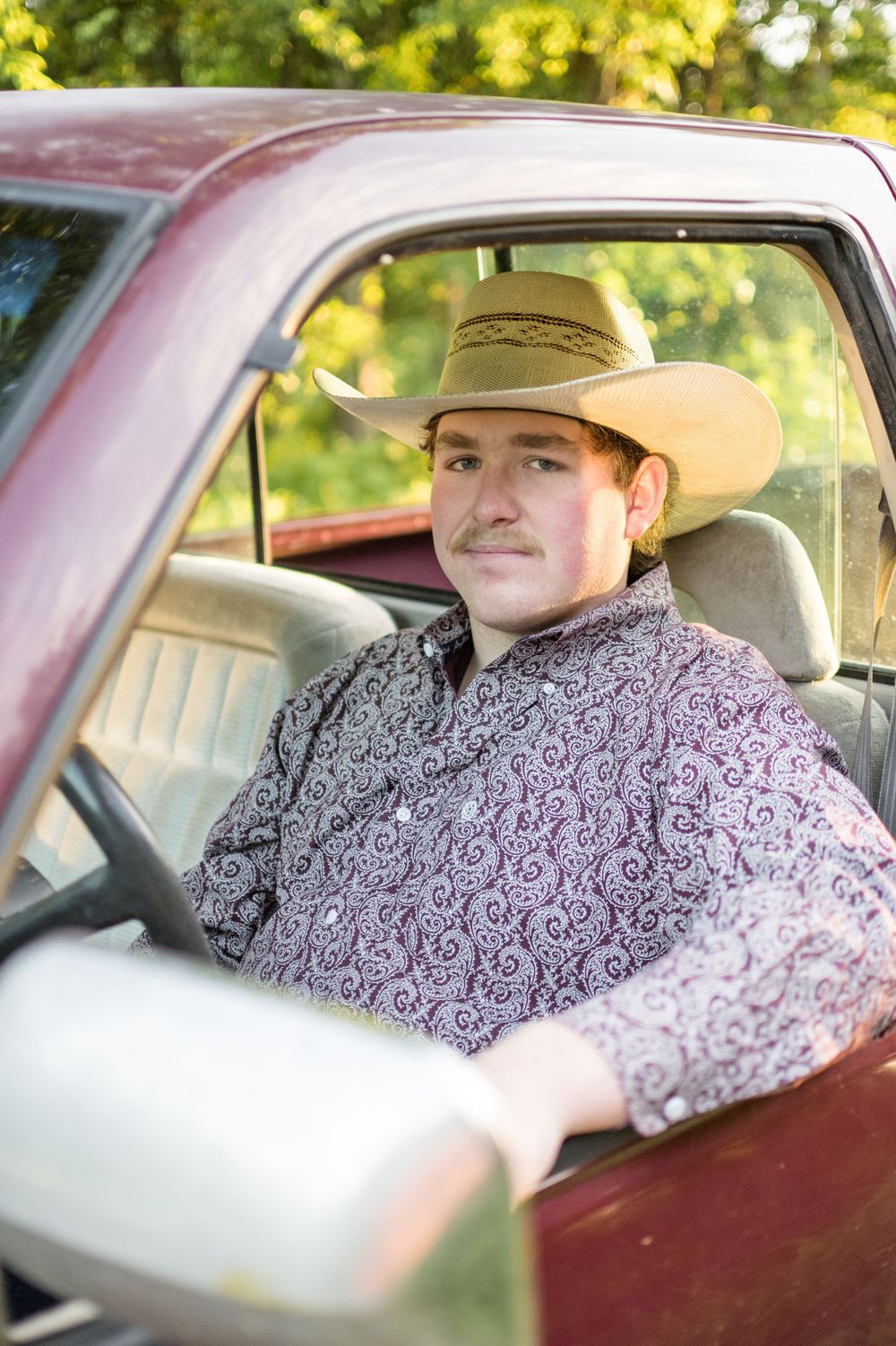 View through truck window shows someone in a patterned purple shirt and cowboy hat sitting in driver's seat.