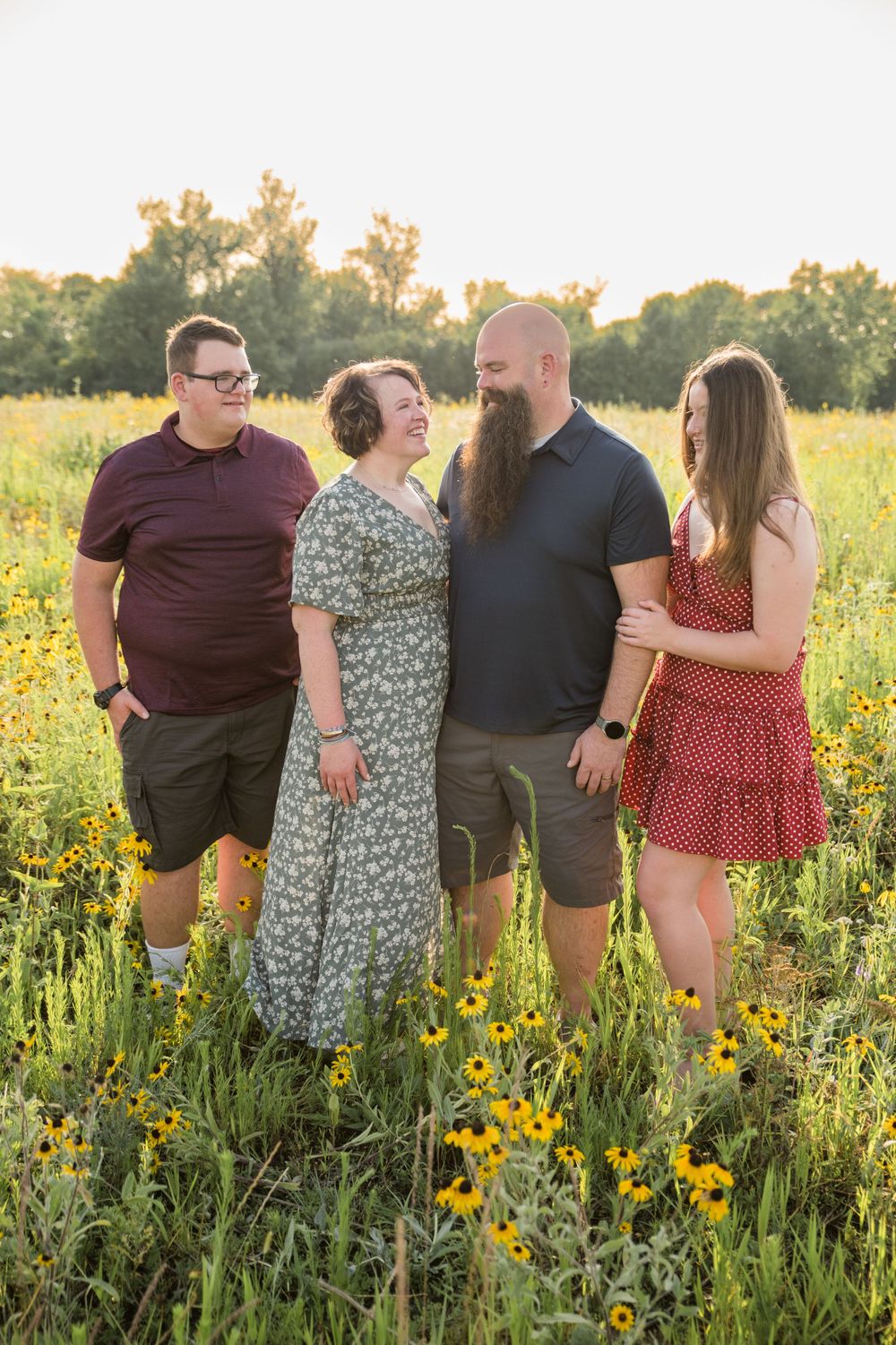 Group in casual attire standing together in a sunny wildflower meadow during golden hour.