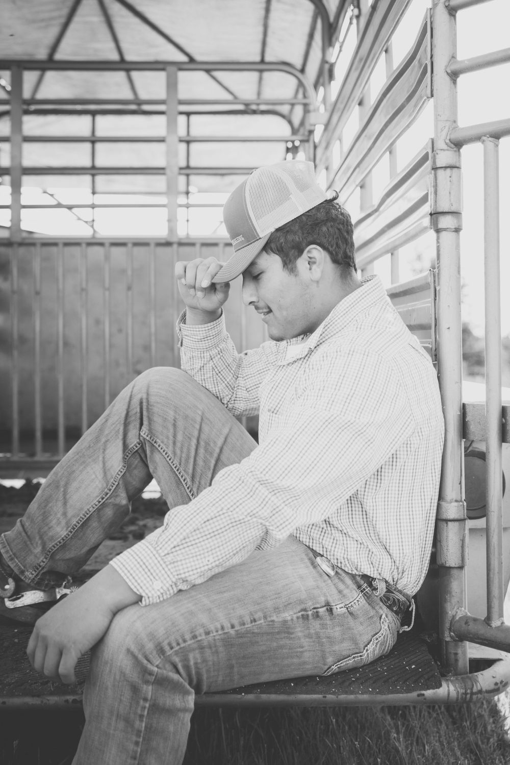 Black and white vintage photograph of someone sitting thoughtfully in casual western attire with a baseball cap.