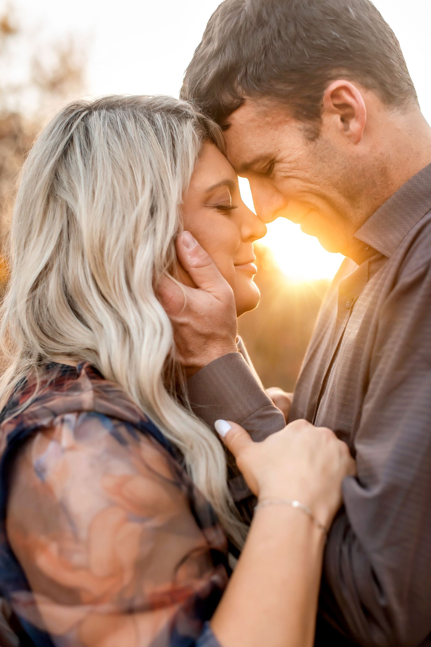 A romantic couple in an intimate moment embrace with golden sunlight glowing behind them at sunset.