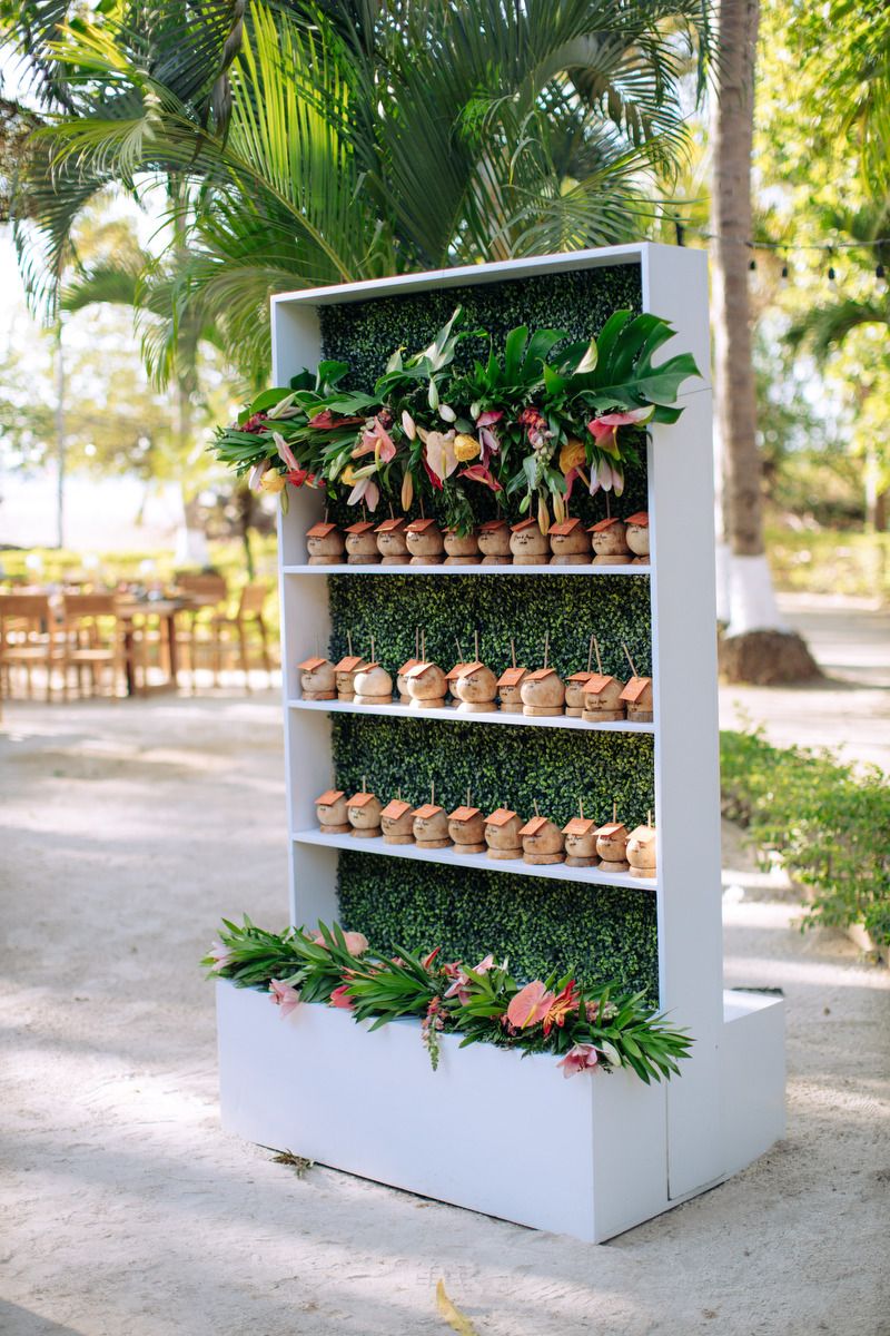 White shelving display with potted plants and tropical greenery at an outdoor wedding venue.