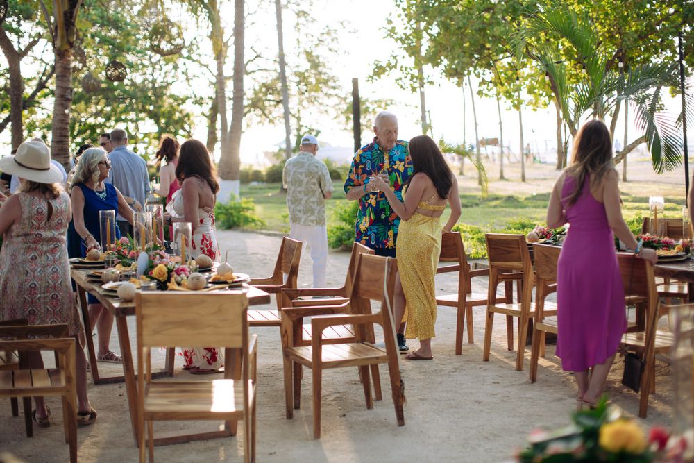 Casual outdoor gathering with wooden chairs and tables set up under trees during daytime.