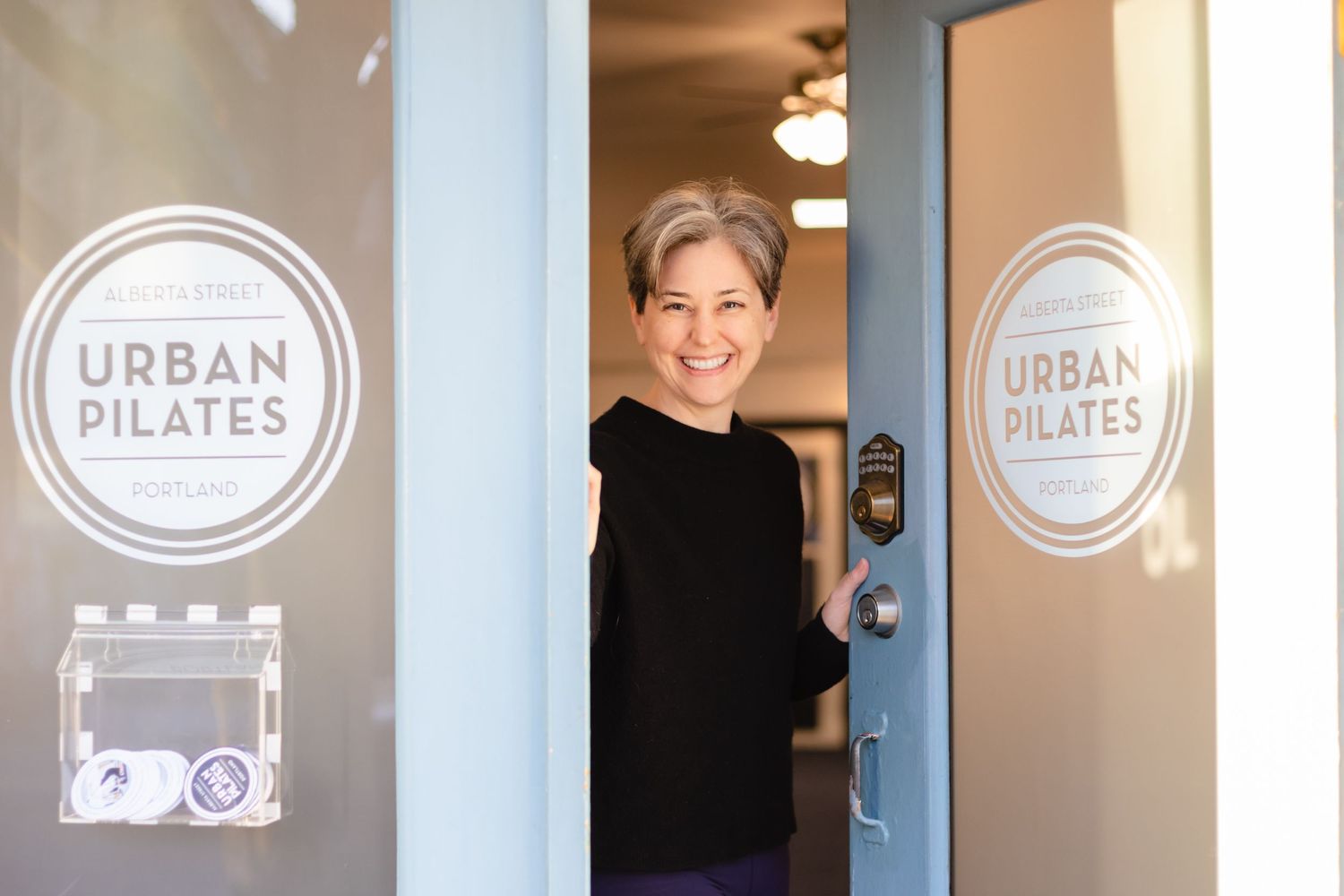 Someone stands in the doorway of Urban Pilates studio with the business logo visible on the glass windows.
