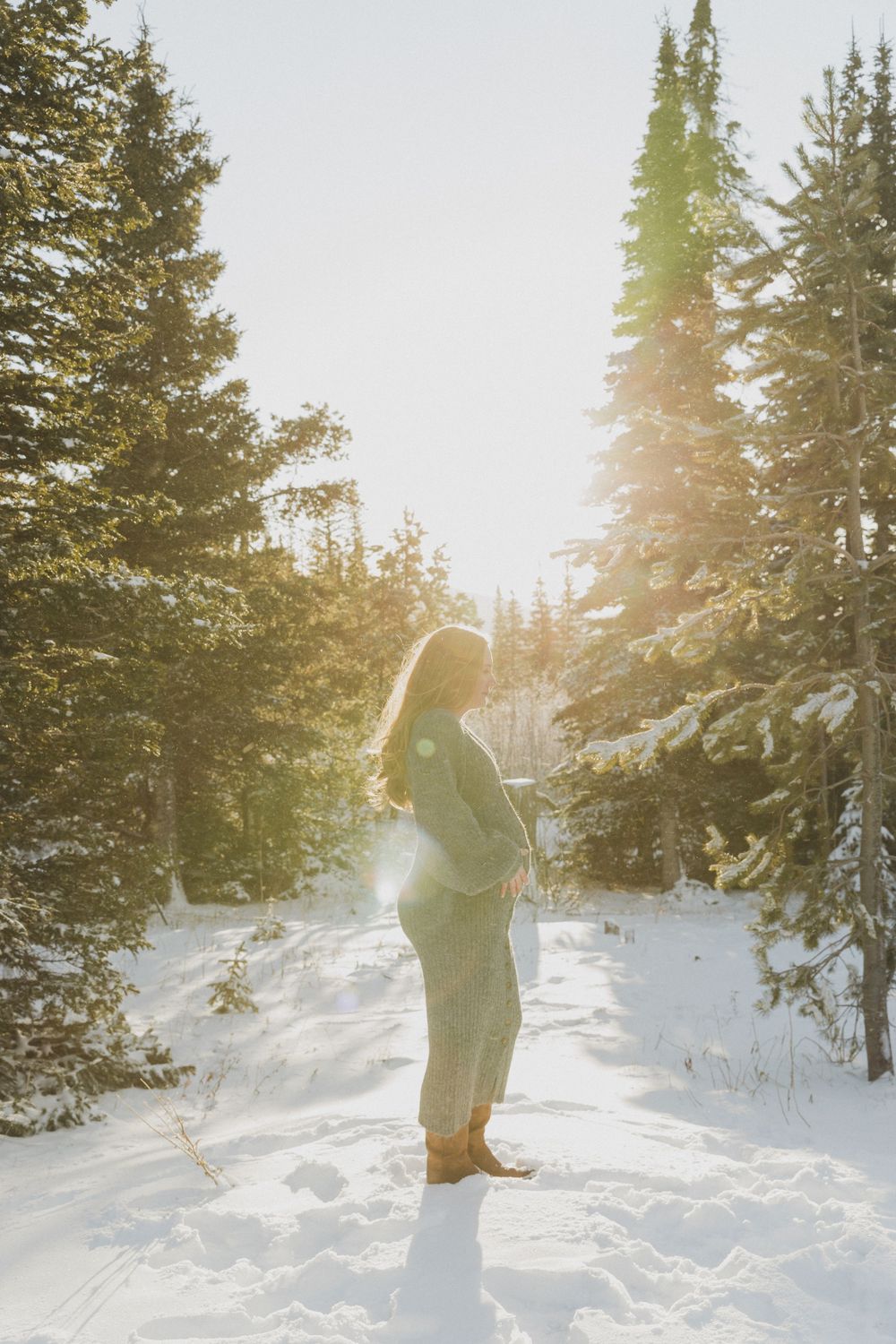 A backlit figure stands in a wintry forest scene with golden sunlight filtering through snow-covered evergreens.