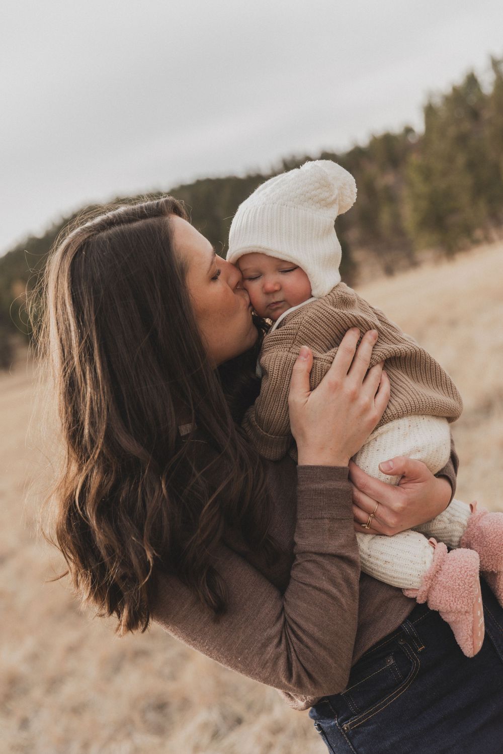 A parent in a brown sweater shares tender moments with a baby wearing a white winter hat in a series of outdoor photos.