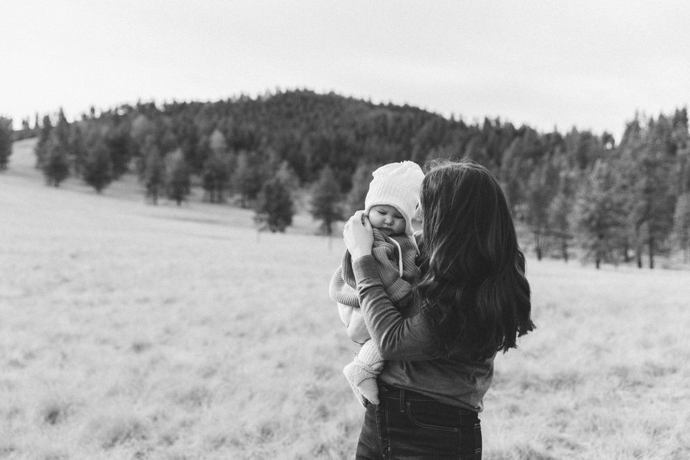 A couple embraces in a romantic black and white outdoor photo series with mountains and fields in the background.