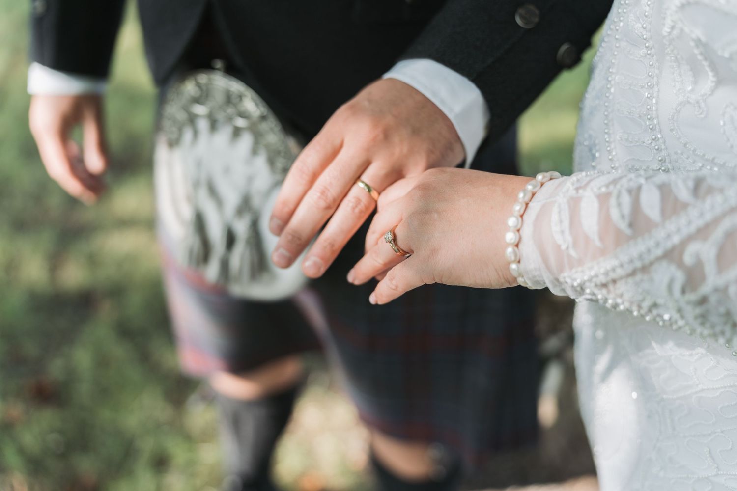 Close-up shot of hands showing off wedding rings with delicate lace detail in an outdoor garden setting.