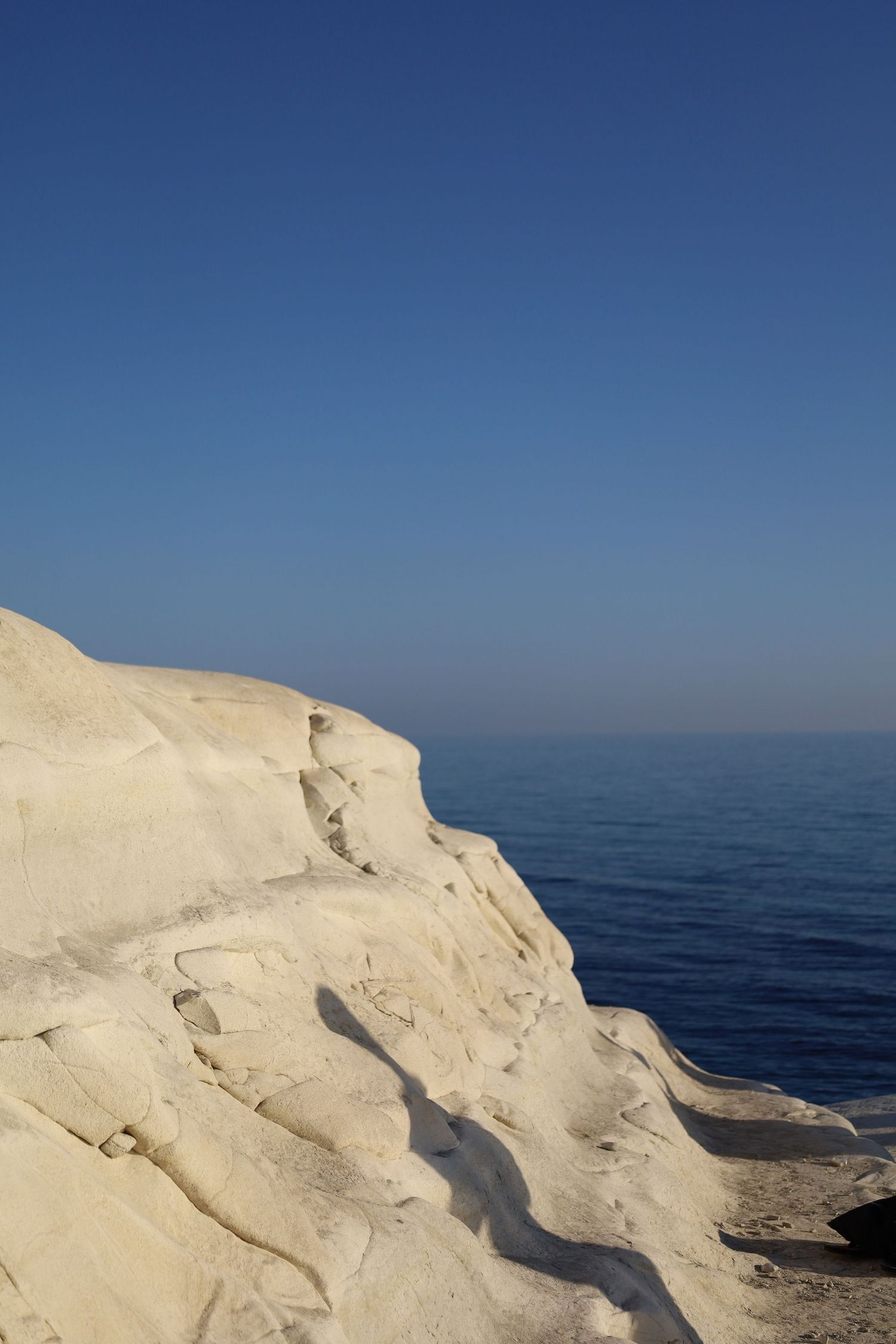 White limestone cliffs meet deep blue Mediterranean waters under a clear sky.