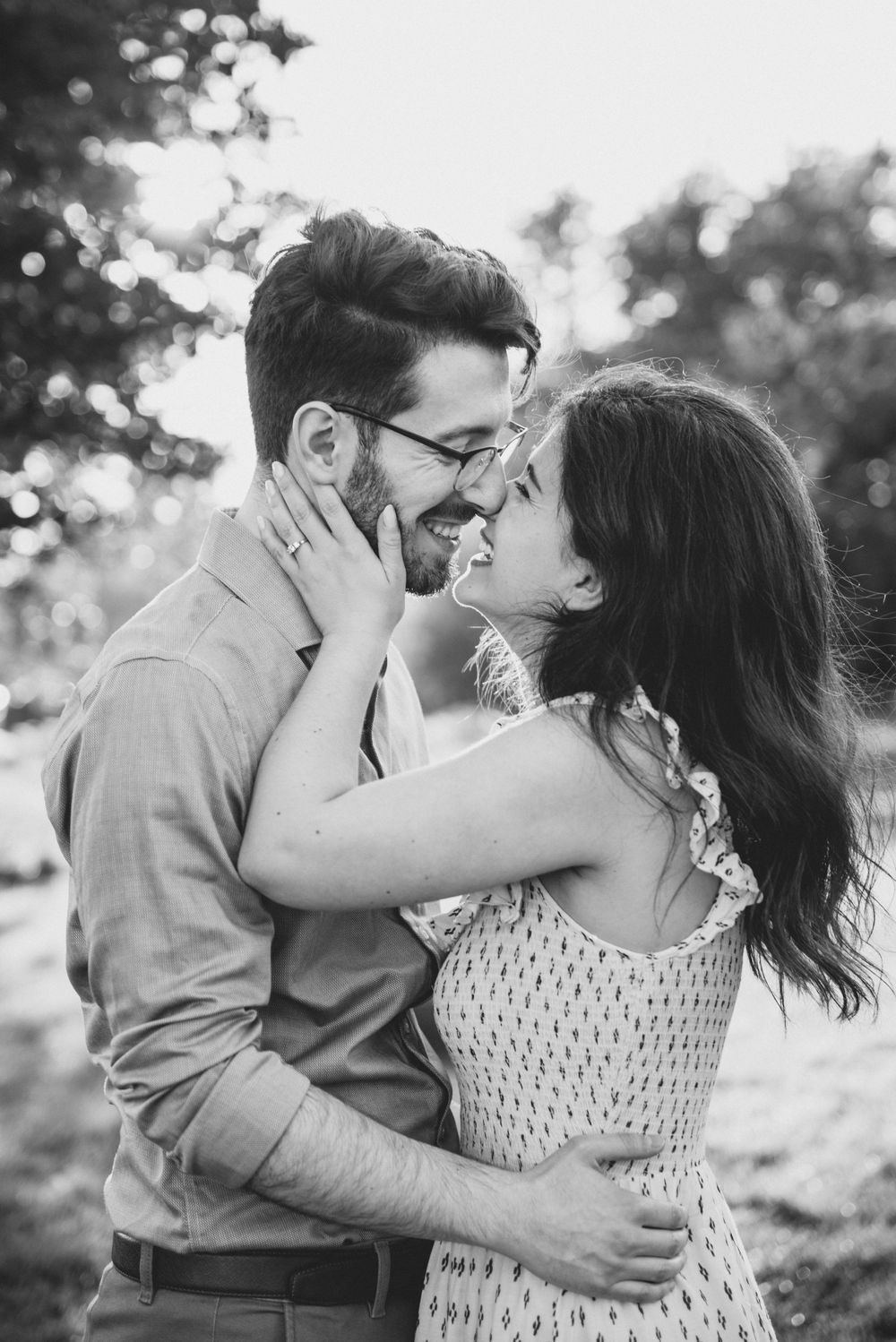 A romantic black and white portrait of a couple embracing and laughing together outdoors in natural lighting.