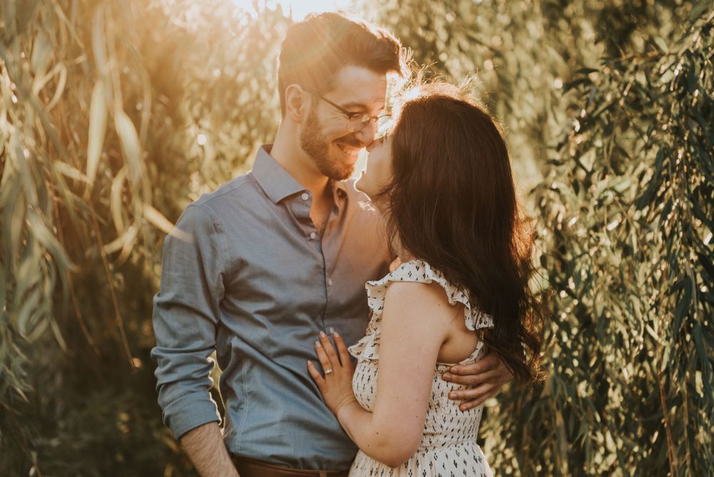 A romantic couple embraces in golden sunlight among green foliage during a sunset photoshoot.