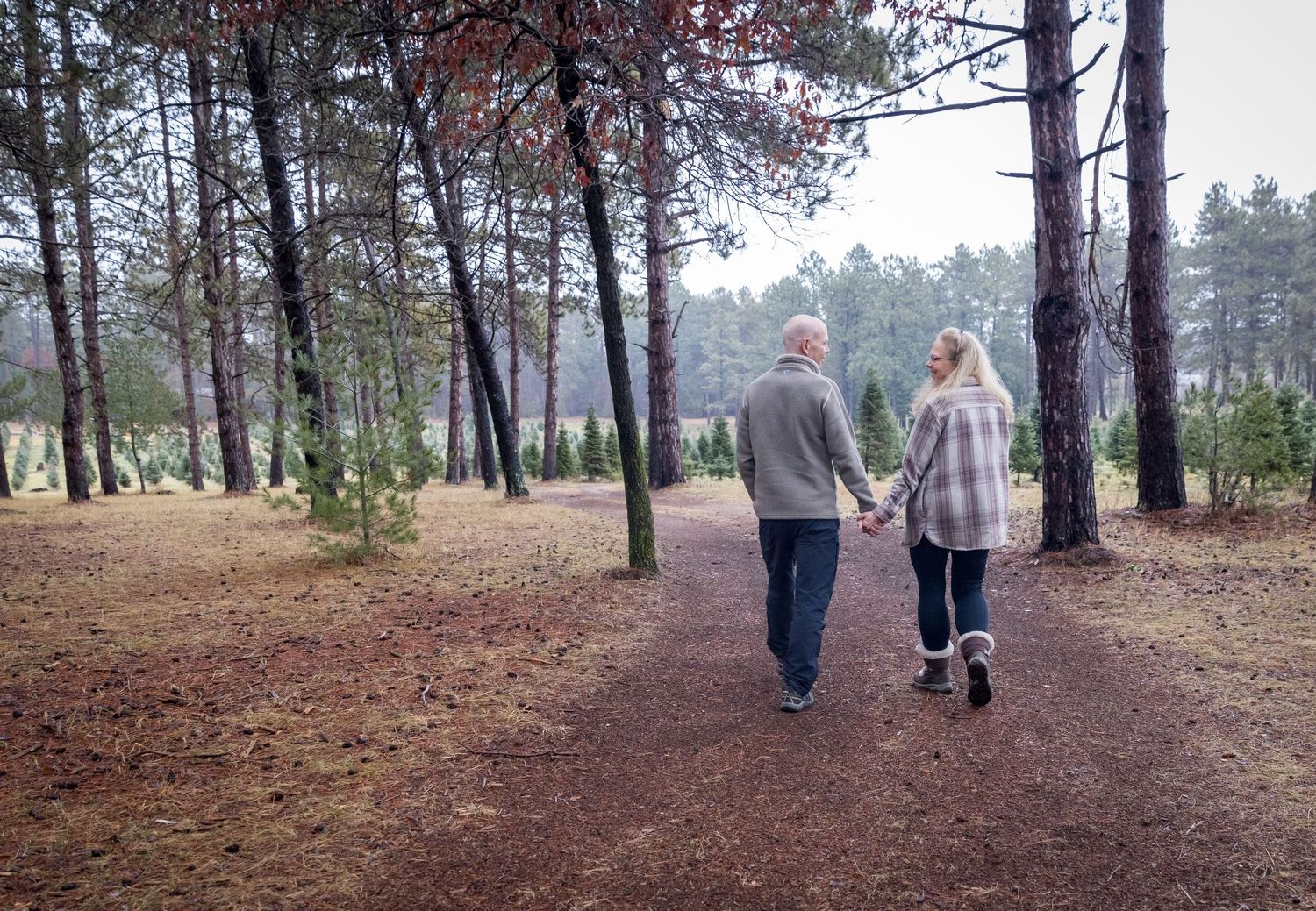 portrait of a couple walking through the tree farm hand in hand