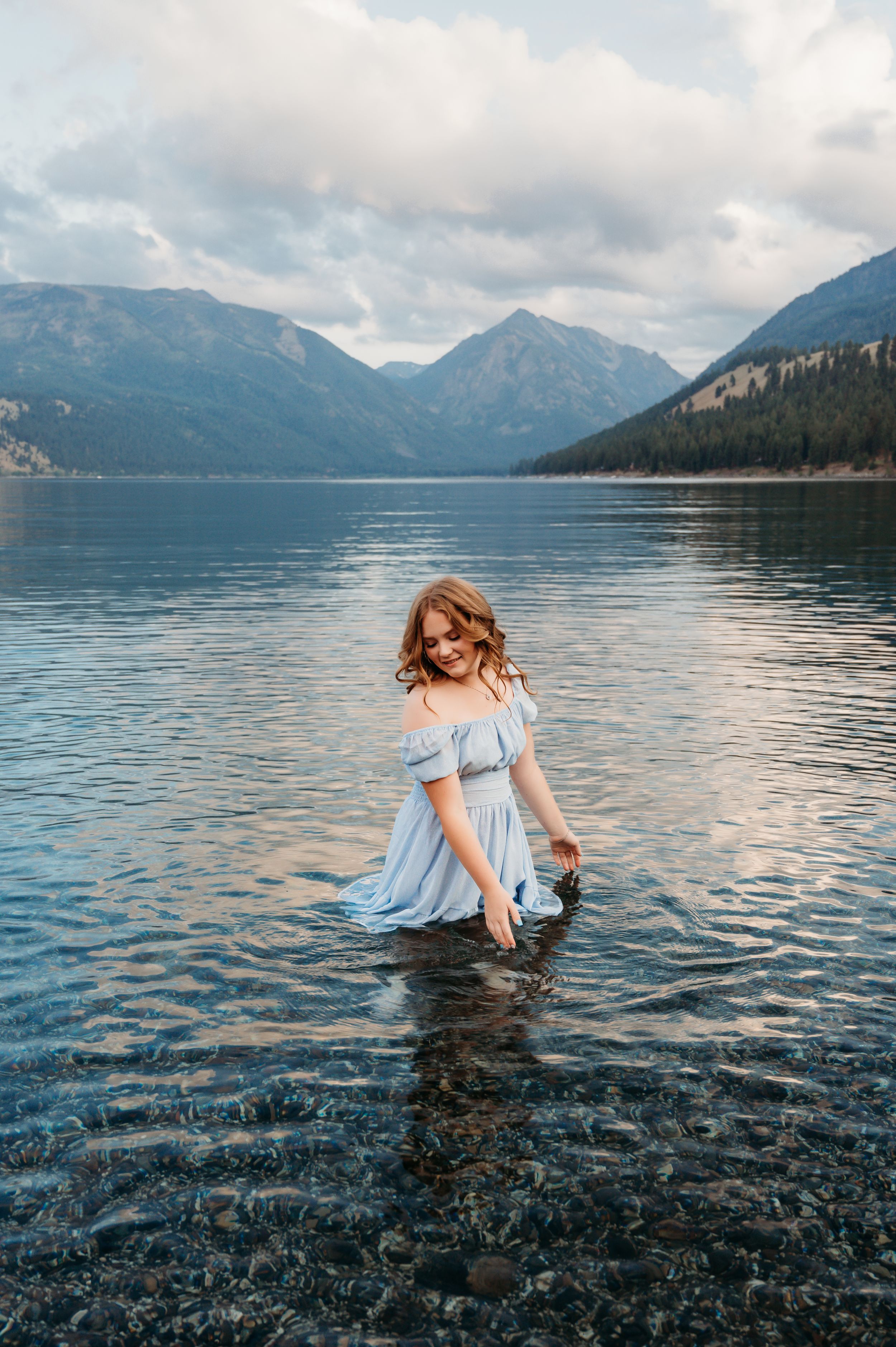 Wading in pristine mountain lake wearing light blue dress at sunset. Wallowa Lake, Joseph, Oregon