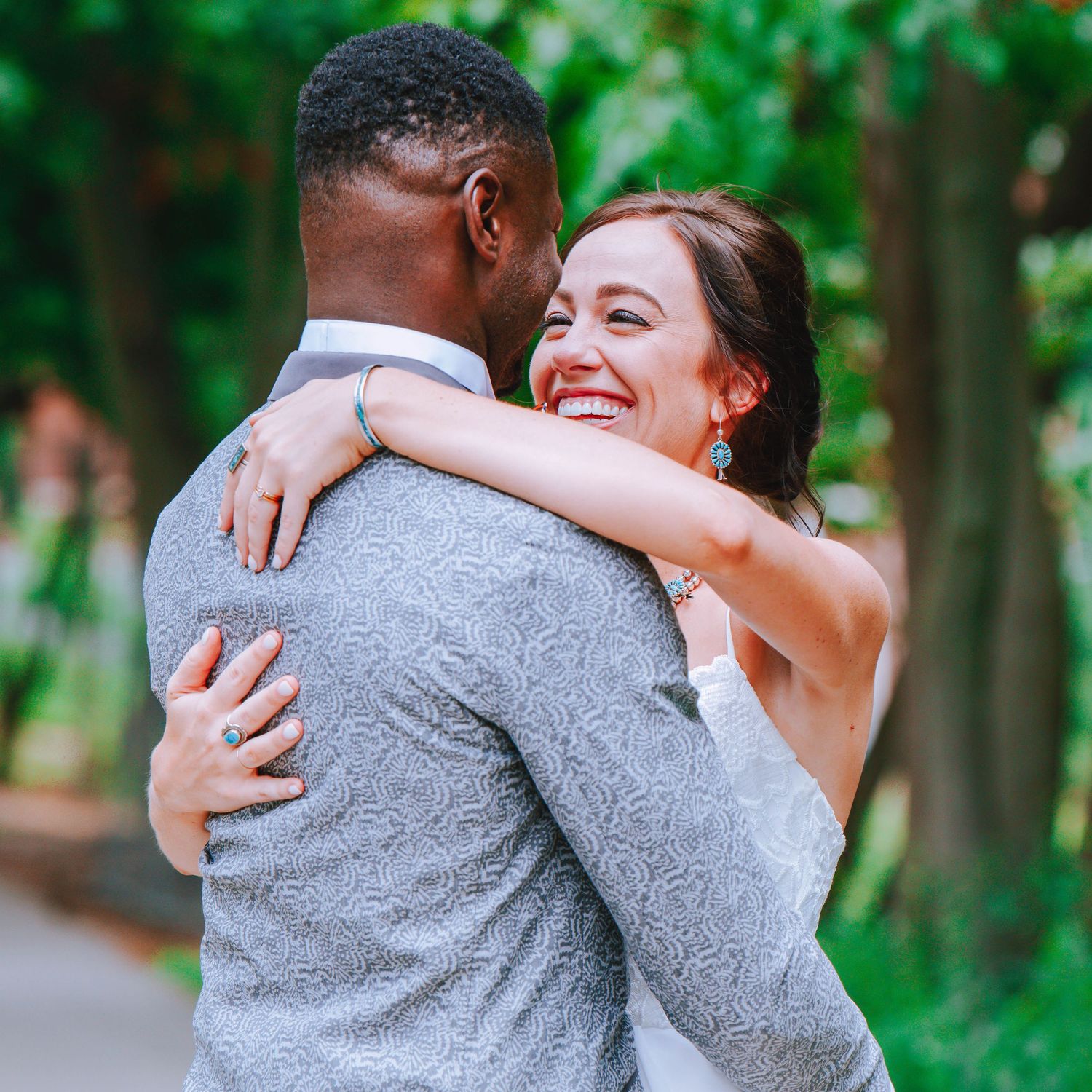 A joyful couple embraces and laughs together during their outdoor wedding photoshoot in a lush green forest setting.