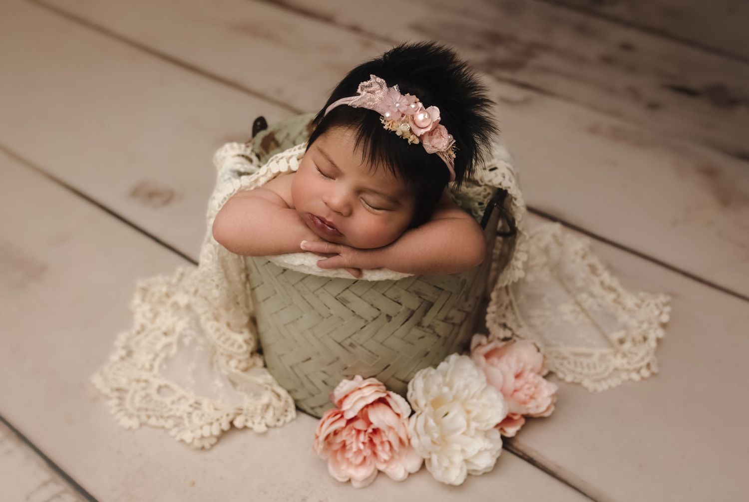 Newborn baby girl with thick brown hair and a pink headband sleeping in a bucket and draped in lace in Charlottesville, Virginia.