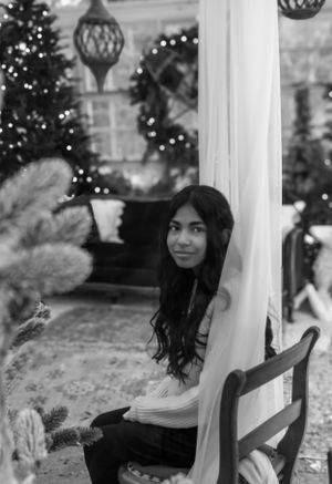 Black and white portrait in holiday setting with Christmas trees and hanging lantern decorations.