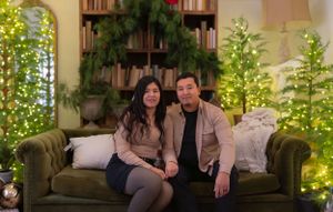Couple sitting on green velvet couch with Christmas trees and holiday decorations in background.